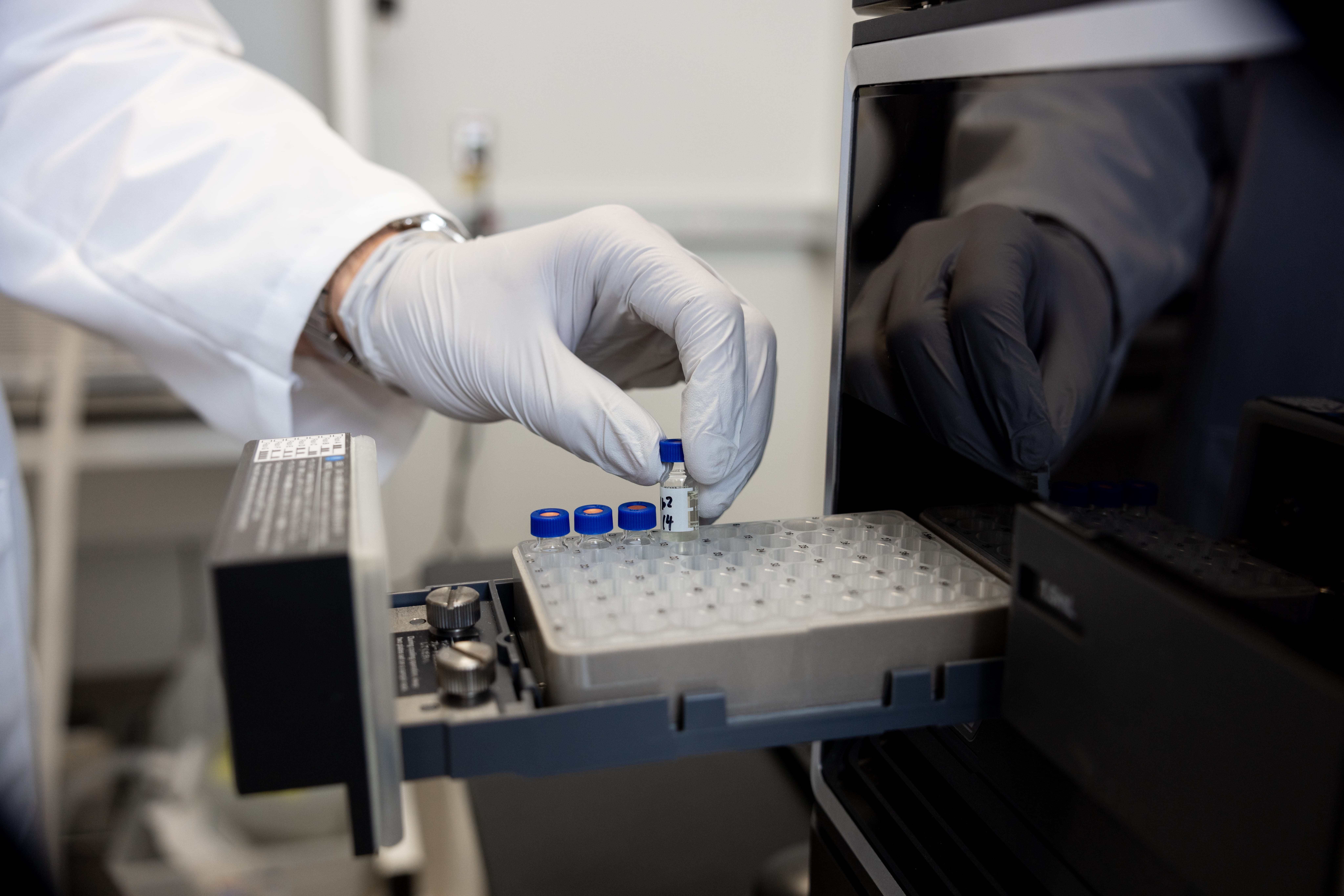 A researcher's gloved hand lifts a glass tube from a tray