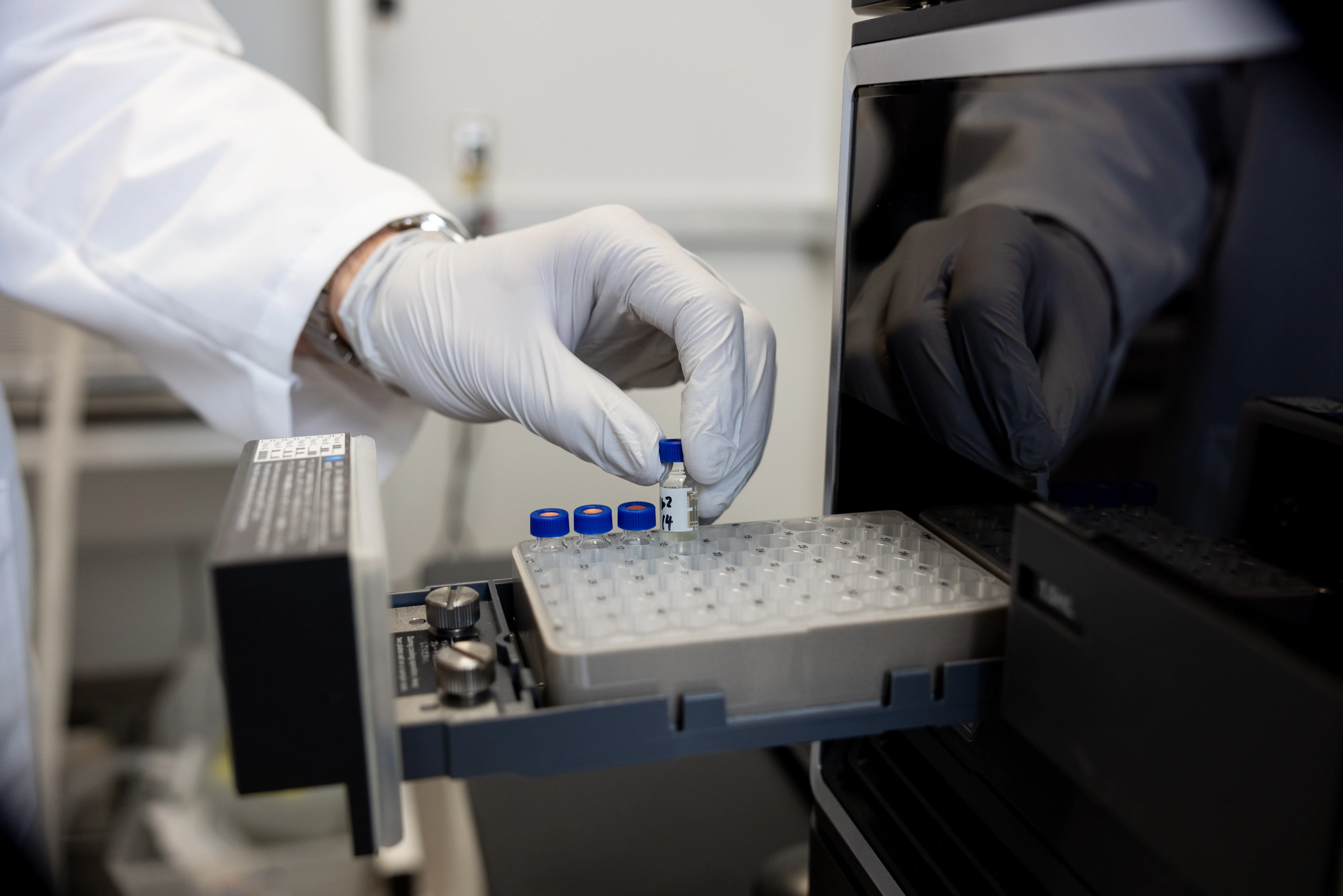 A researcher's gloved hand lifts a glass tube from a tray