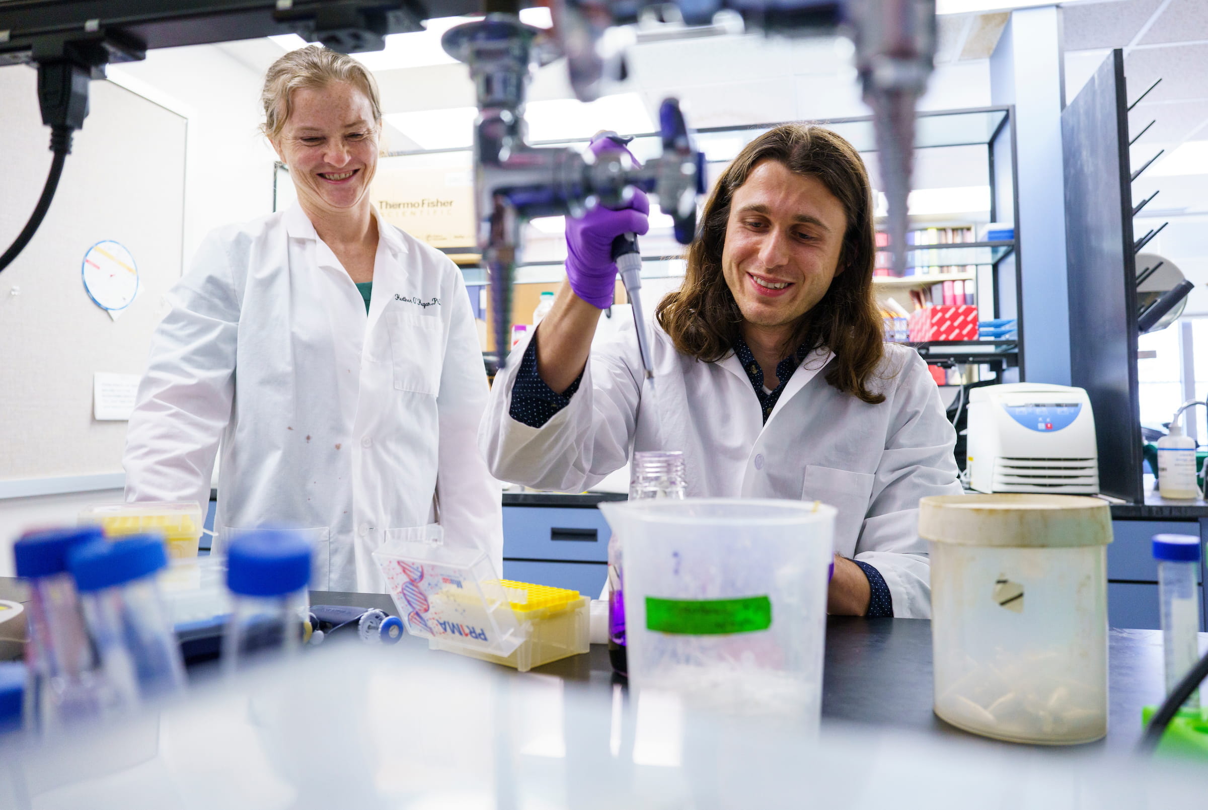 A woman watches a man work on lab equipment.