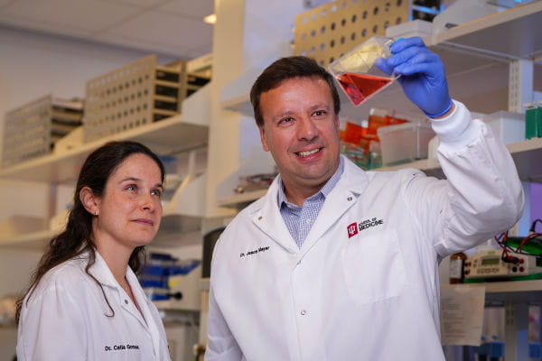 two professors in lab coats in lab looking at liquid in glass 