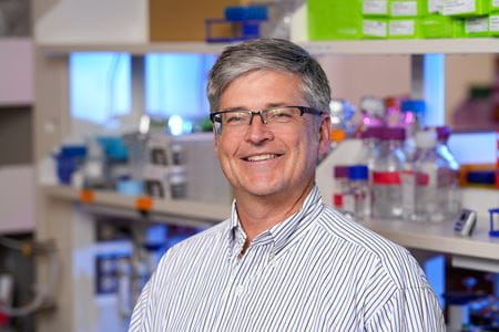 A man wearing glasses is photographed in a laboratory.