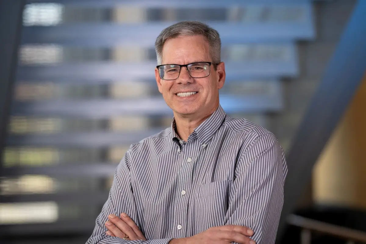 John Turchi poses with his arms crossed, standing beneath a staircase