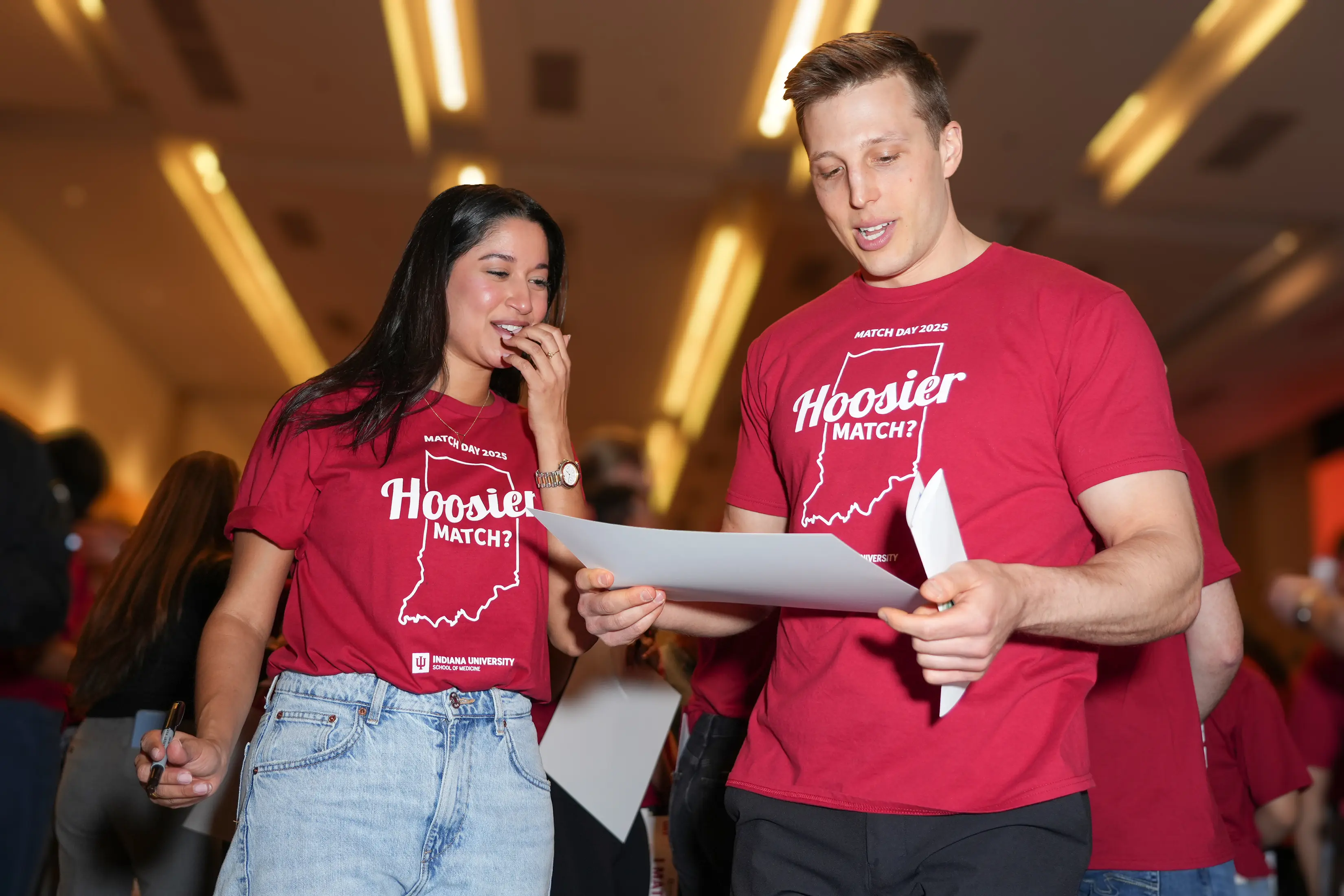 A woman holding a marker looks at a man holding a piece of paper. 