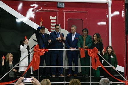 Several adults cut a ribbon in front of a large red truck.