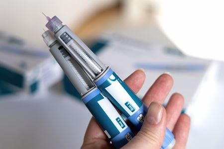 A hand holds two semaglutide injectors.