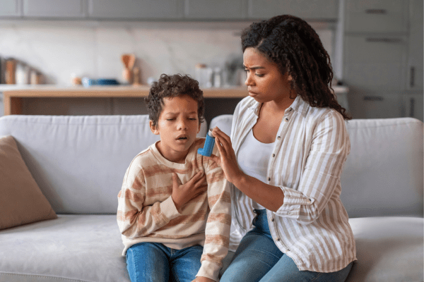 Stock photo of a young boy receiving inhaler help from his mother