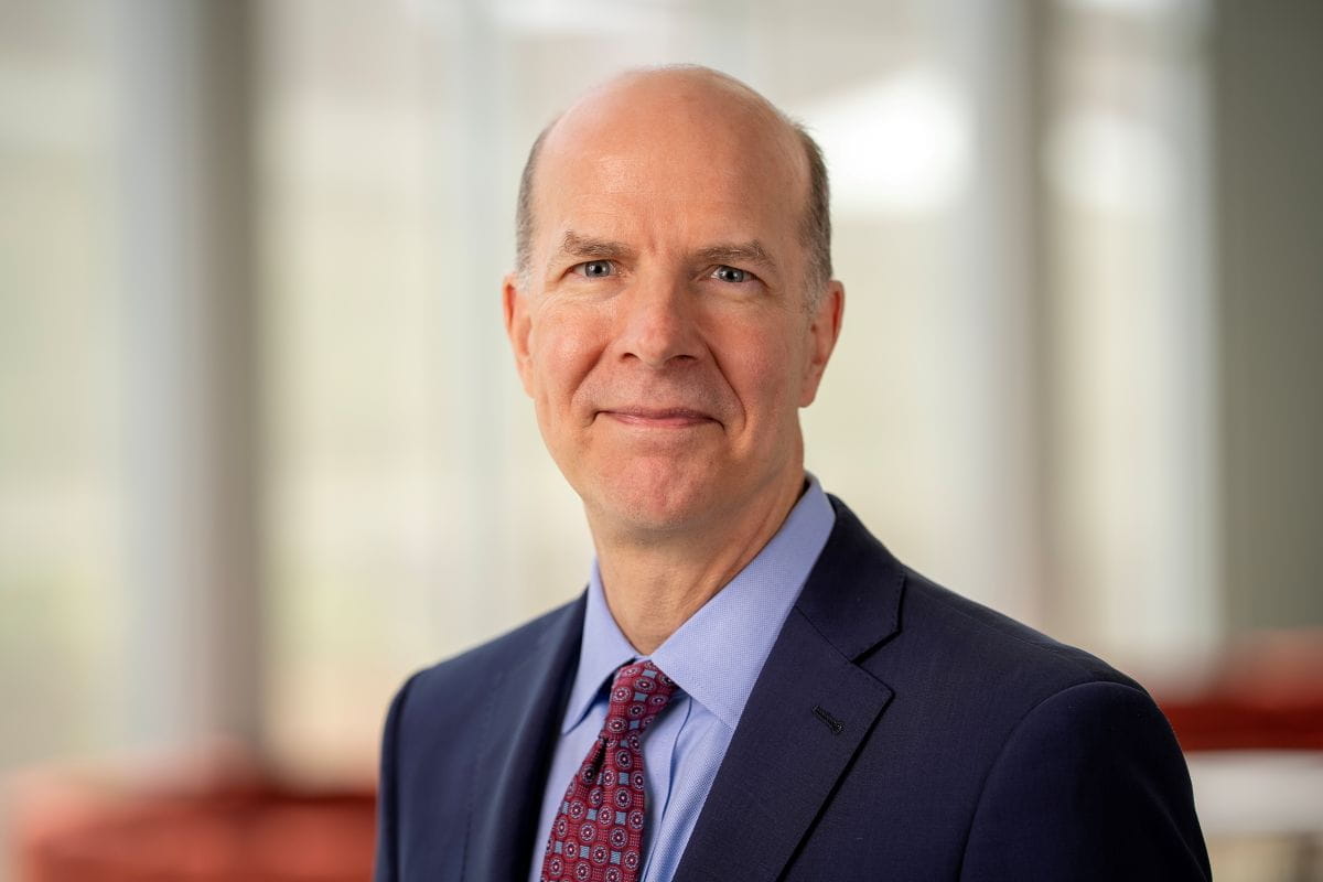 A man in a suit poses for a headshot. 