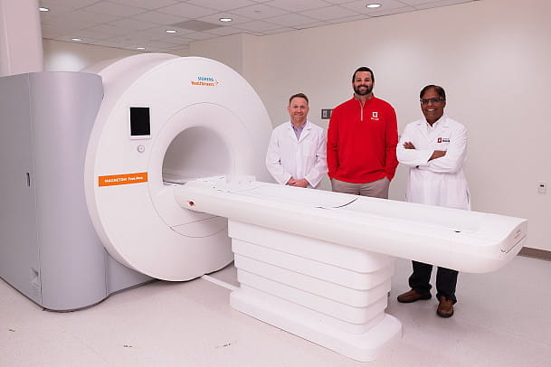 Three men stand next to an MRI machine. 