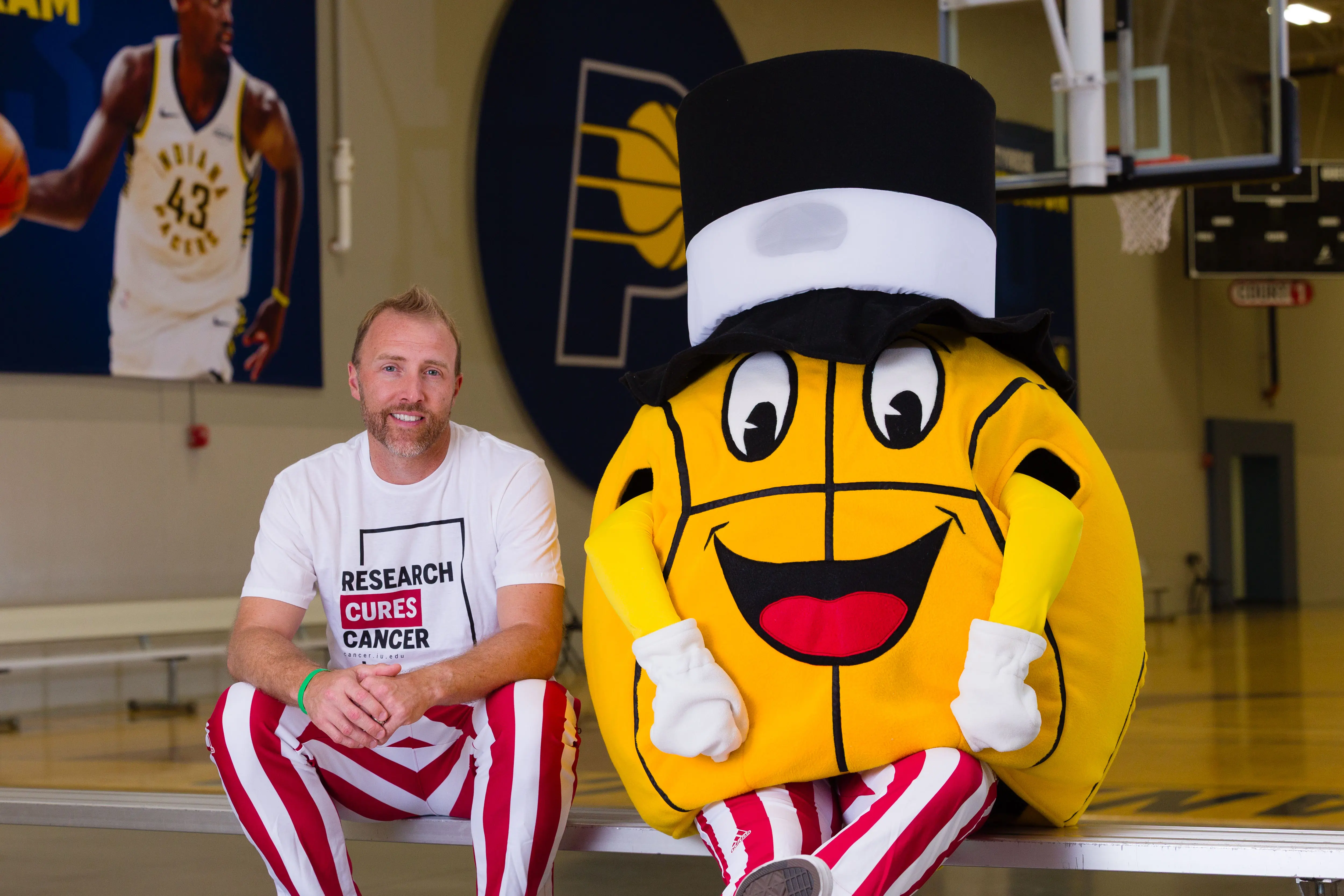 A man sits with a basketball mascot