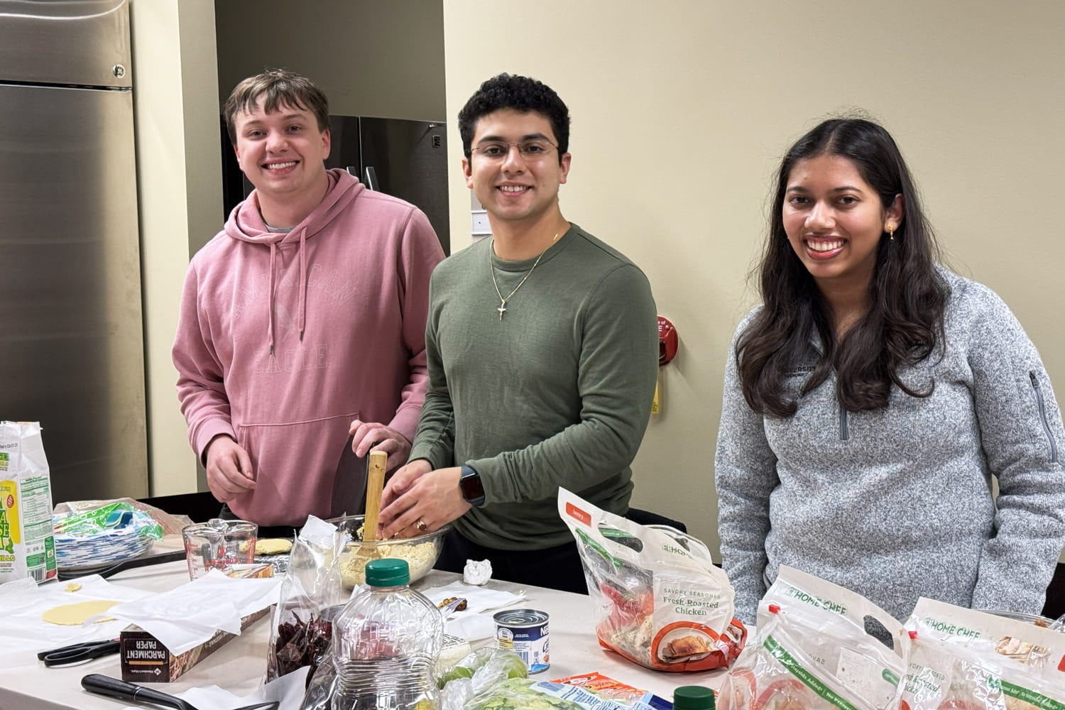 Three students smile while working to prepare a meal in the teaching kitchen on the West Lafayette campus