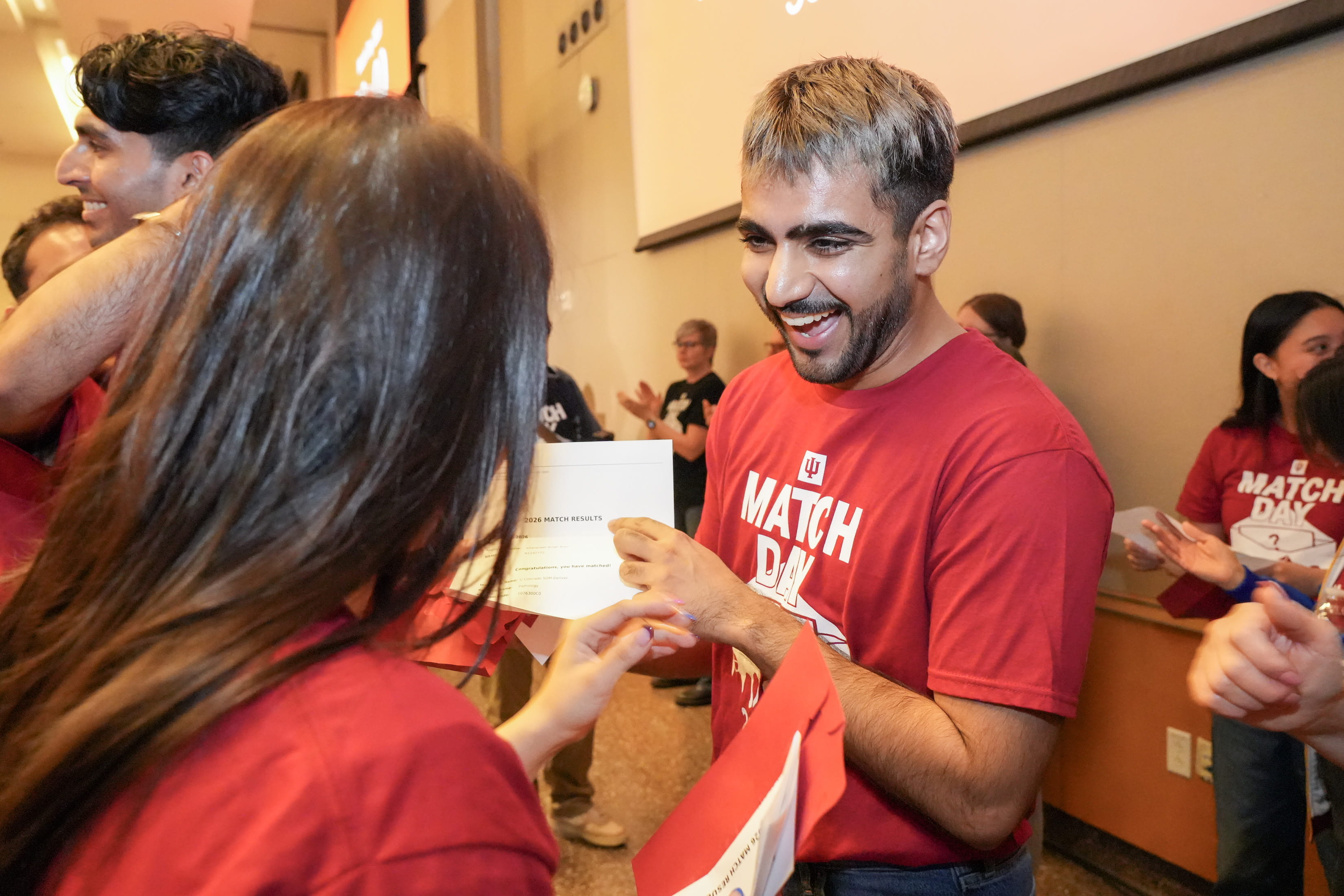 A man in a red shirt holds up a white piece of paper. 