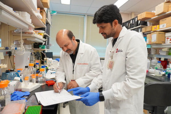 two people in white coats in lab looking at notebook
