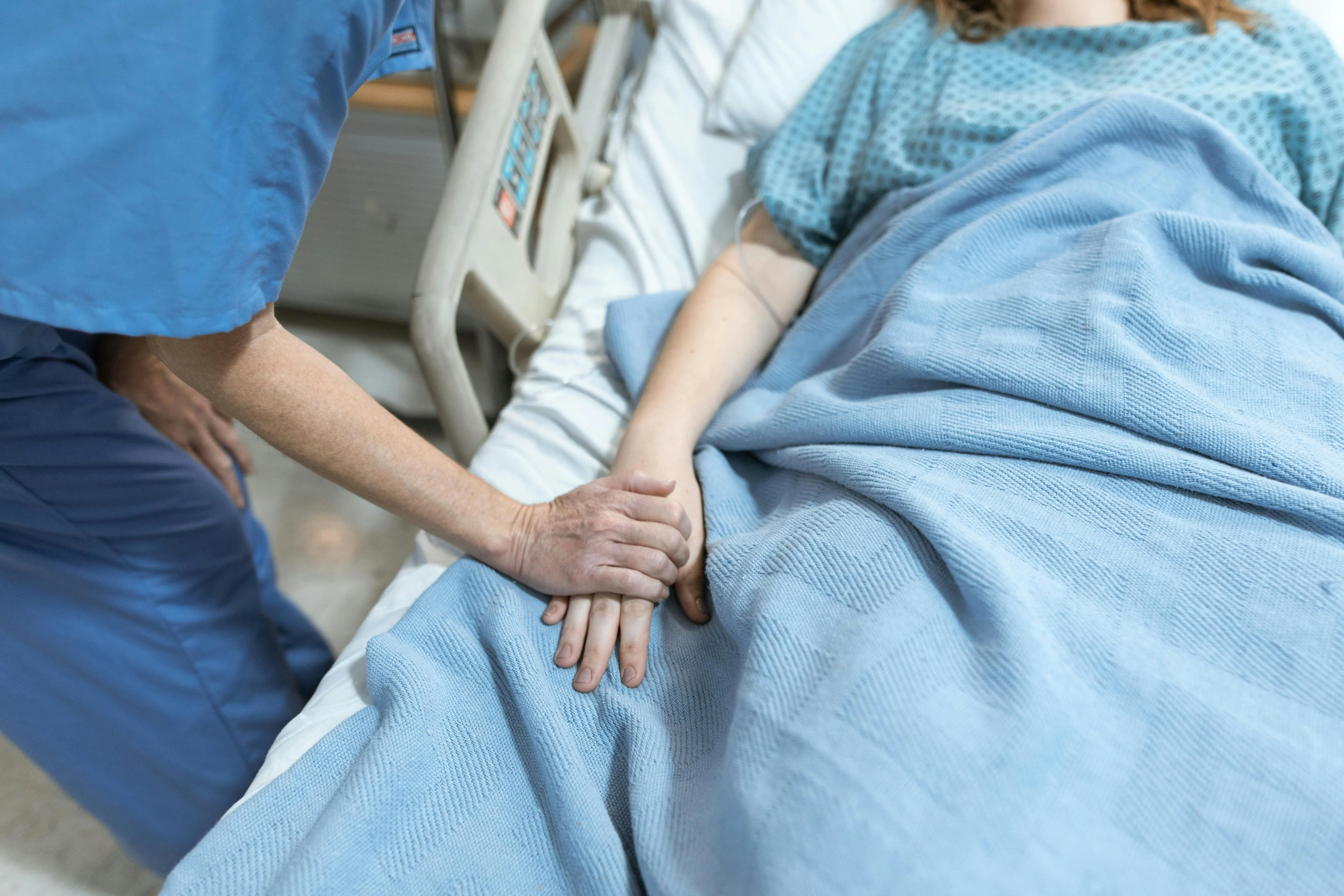 A nurse holds the hand of a patient who lies in bed.