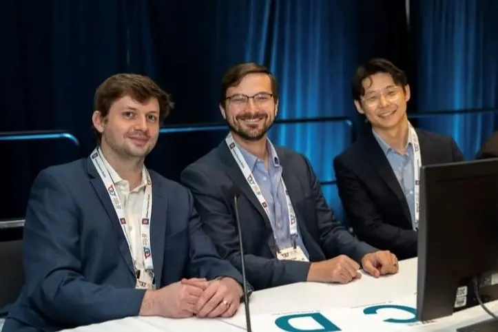 Three individuals wearing conference badges sit at a table with microphones, facing the camera during a panel discussion.
