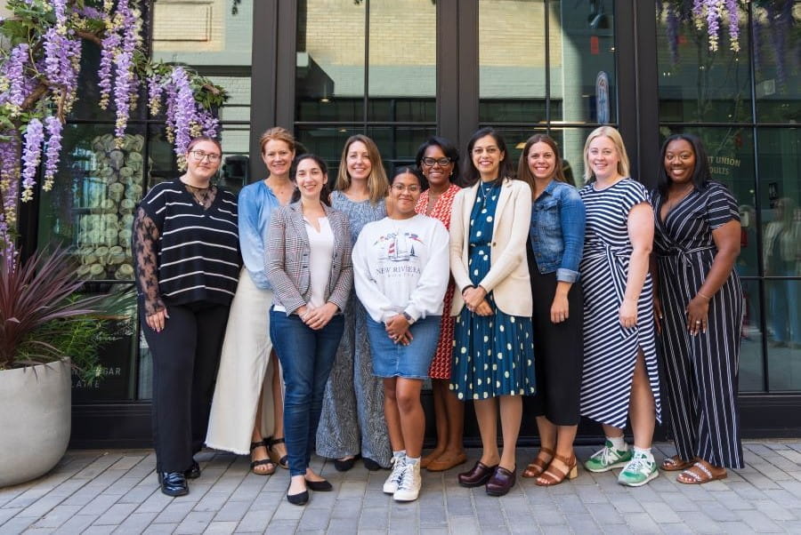 A group of women stand outside where there are lavender flowers framing the picture.