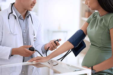 Pregnant person having blood pressure measured by doctor