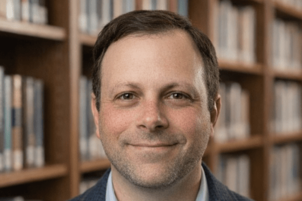 Adam Comer headshot up against a bookshelf 