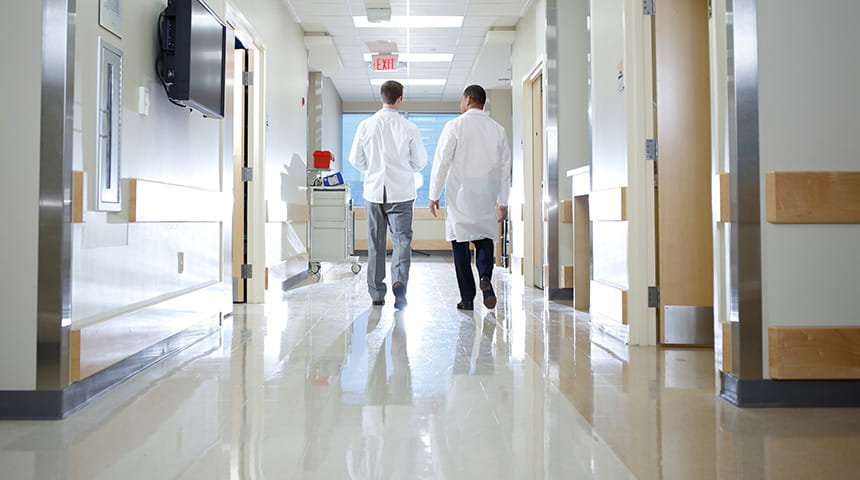 a physician and medical student walk down a hospital hallway