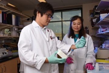 two researchers in white coats work together in the lab