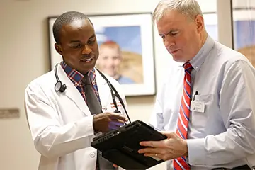 Two male physicians chatting while one holds a clipboard
