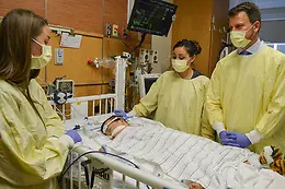 Three health care providers looking over a child in a hospital bed under critical care