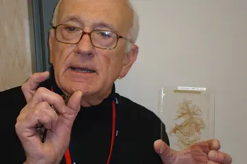 A researcher holds a bio sample in one hand while speaking and gesturing with his other hand.