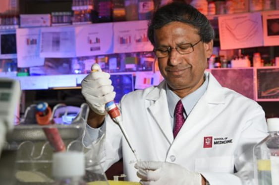 debomoy lahiri pipettes a sample in the lab while wearing a lab coat and gloves