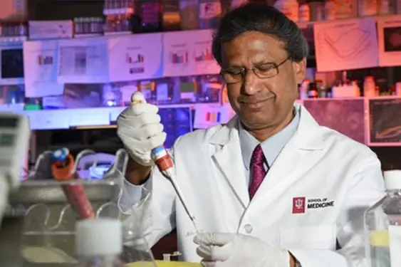 debomoy lahiri pipettes a sample in the lab while wearing a lab coat and gloves