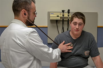 a resident checks a patient's lungs with a stethoscope during a clinical visit