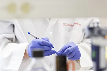 Up close view of gloved hands using a sharpie to mark a sample in the lab