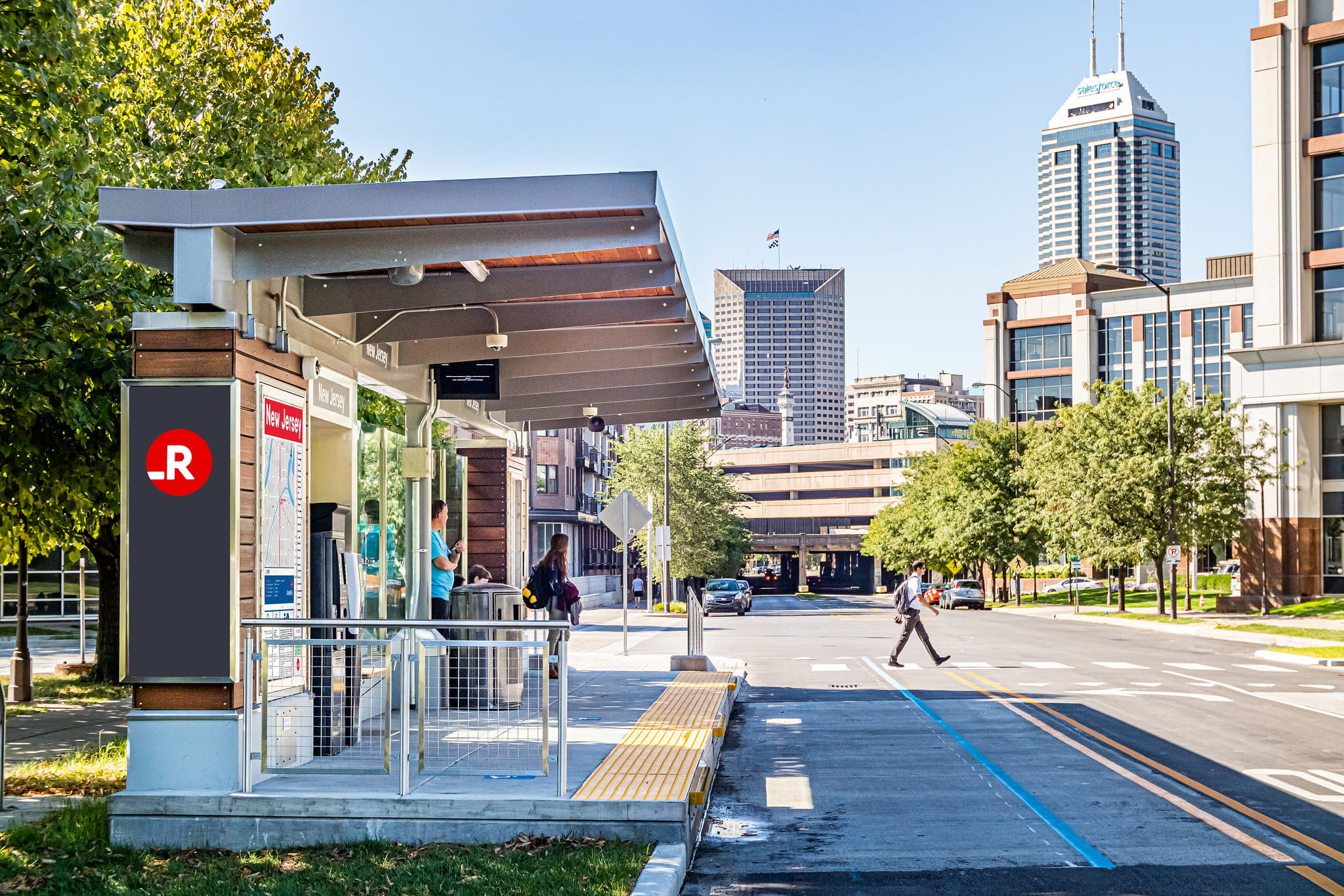a bus station in front of the indianapolis sky line with a pedestrian crossing the street