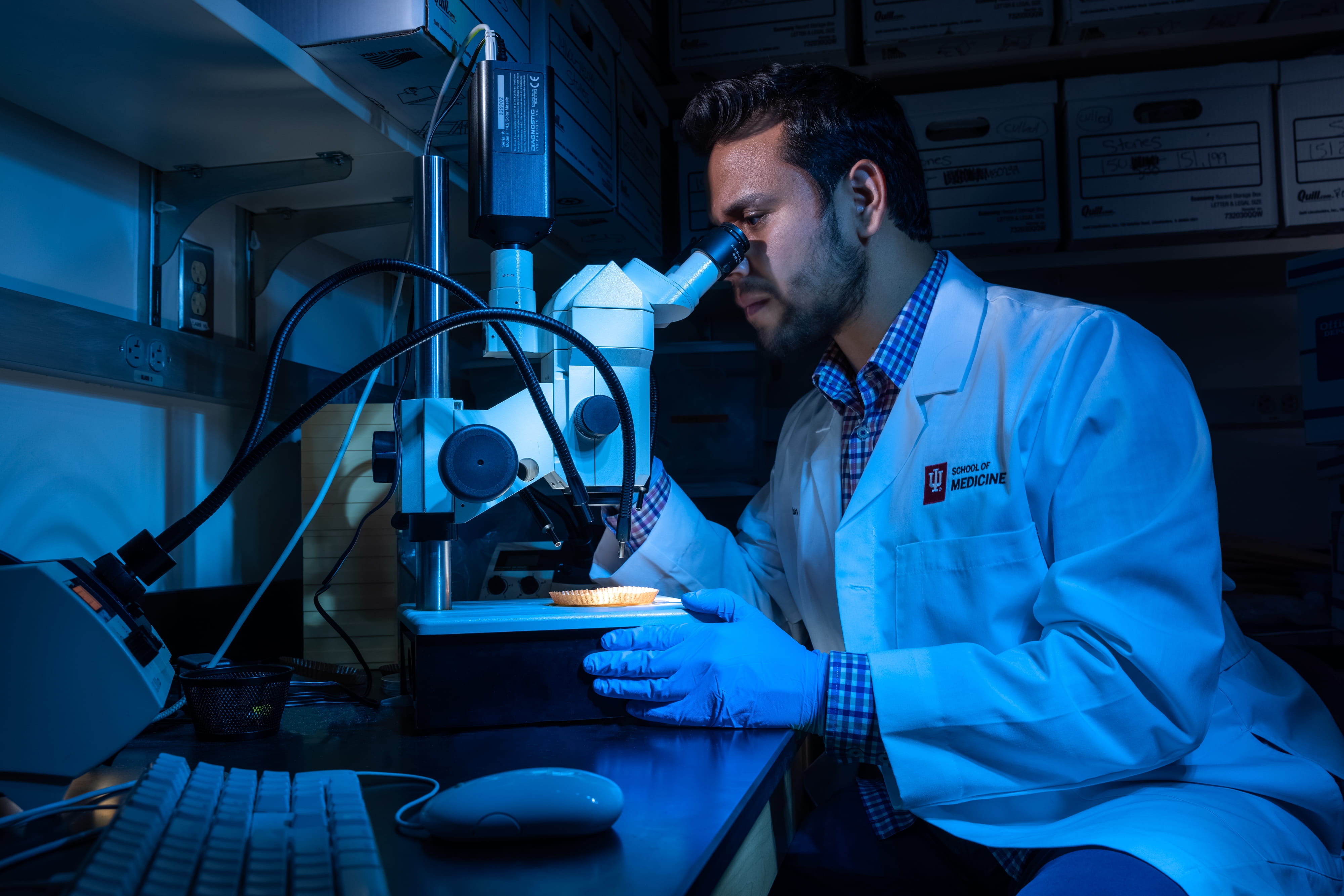 victor canela looks into a microscope in a dark lab