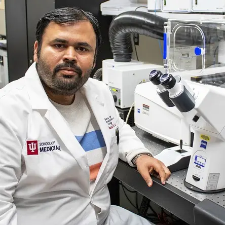 A postdoctoral fellow wearing a lab coat sits in front of a microscope