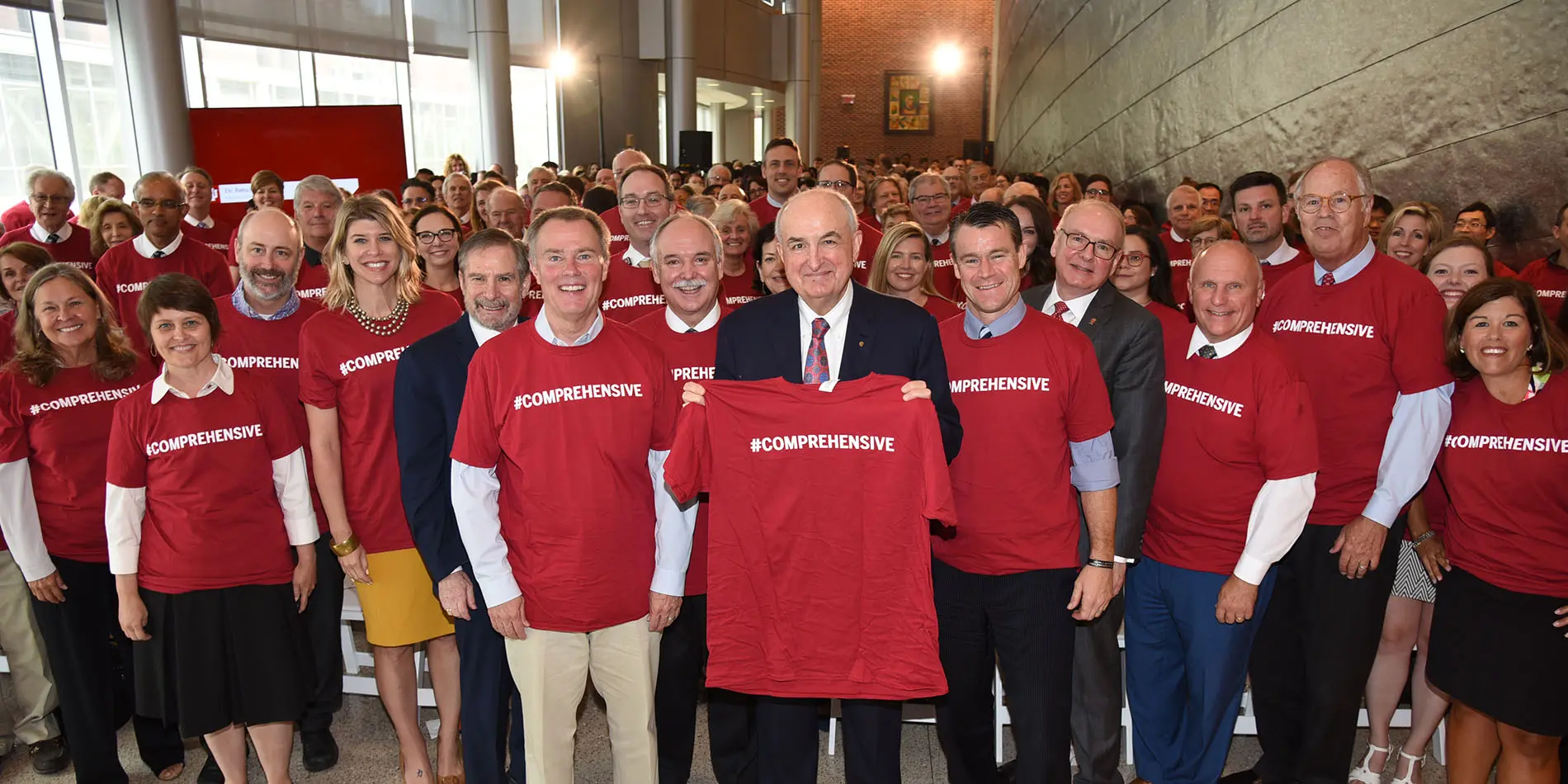 Hundreds of people at the cancer center celebration all wear red t-shirts with text reading #comprehensive