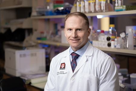 A man in a white lab coat poses in his lab.