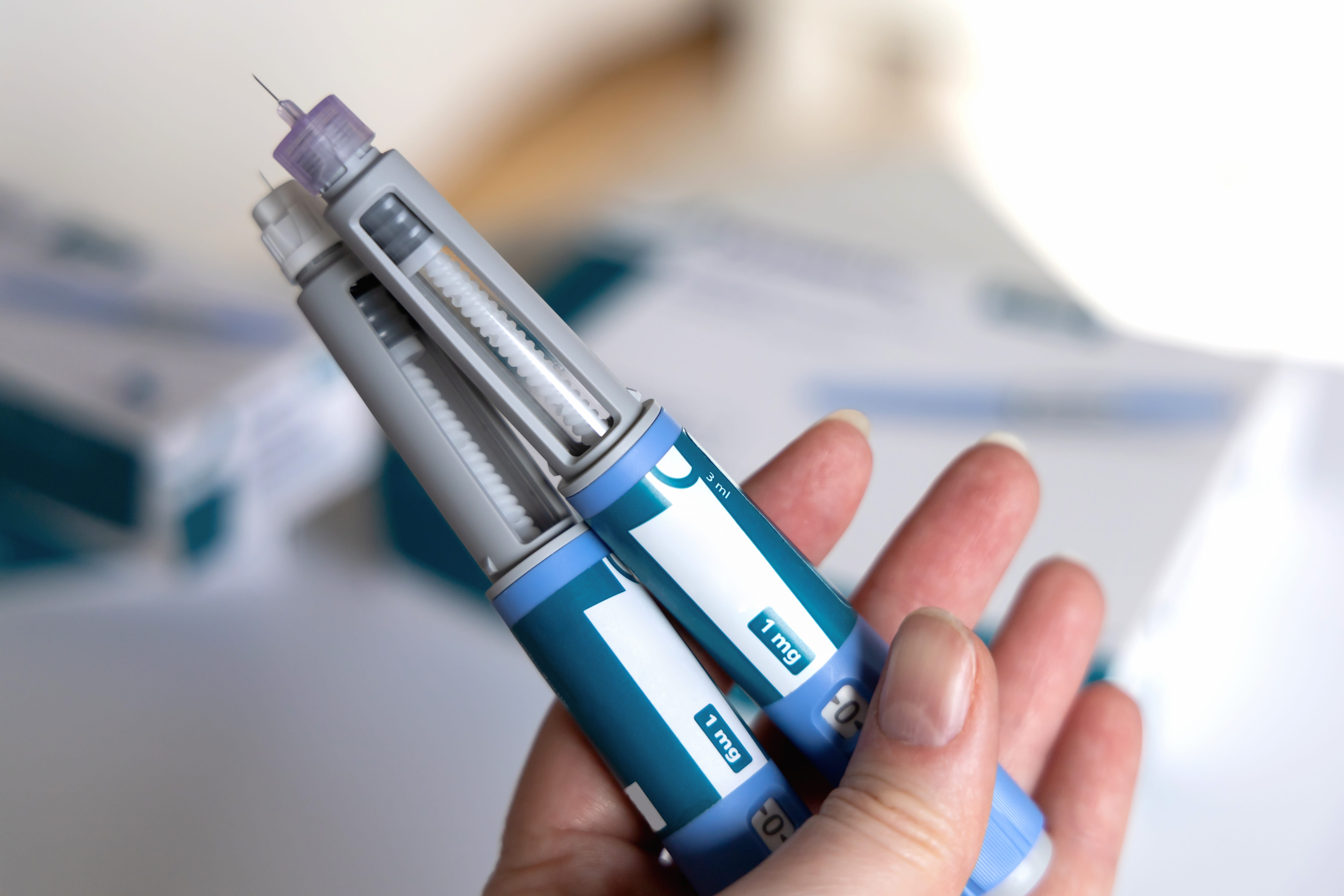 A hand holds two semaglutide injectors. 