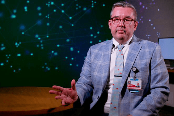 Anthony Shanks, MD, MEd, sits in a checkered suit before a starred background.