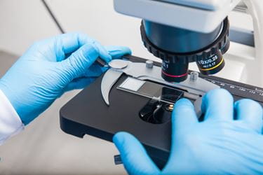 doctor with gloves on and hands on microscope