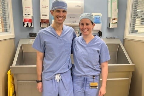 Orthopaedic Surgery Trauma fellows, Tim Murphy and Michelle Lawson, pose in their surgical scrubs in front of the sink where they scrub in.